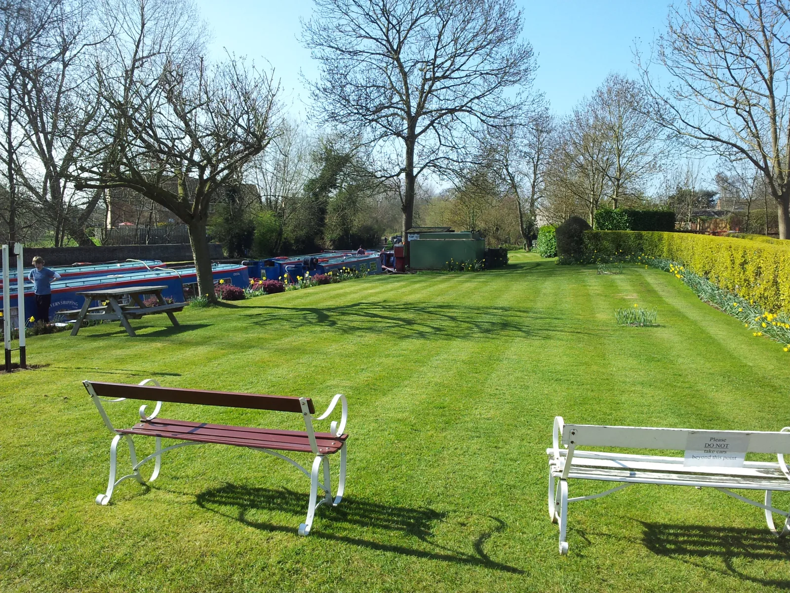 The shared lawn at Waterside Cottage with a bench and boats moored beyond the trees