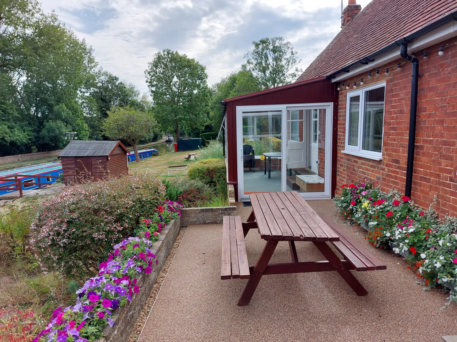 Terrace outside Waterside Cottage with a picnic table and flower beds in bloom