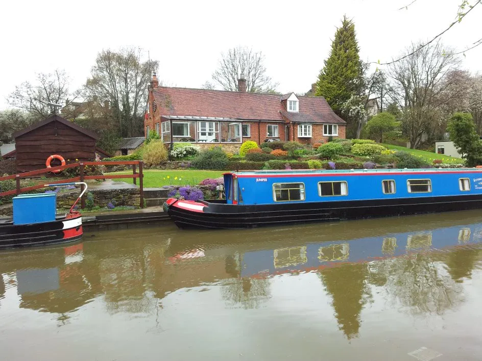 Blue narrowboats moored below Waterside Cottage with its garden running down to the water