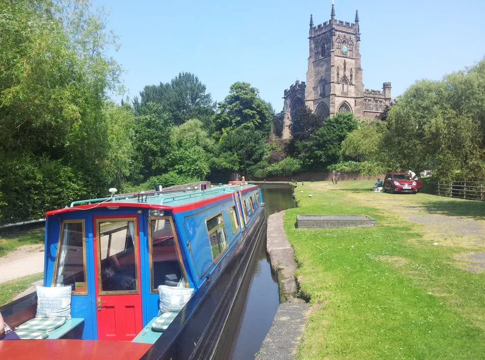 Narrowboat on the towpath with a church tower rising behind the trees