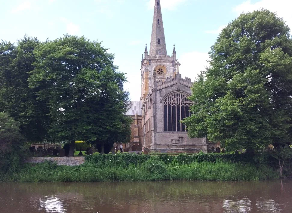 Large stone church with a tall spire seen across the water from a canal boat