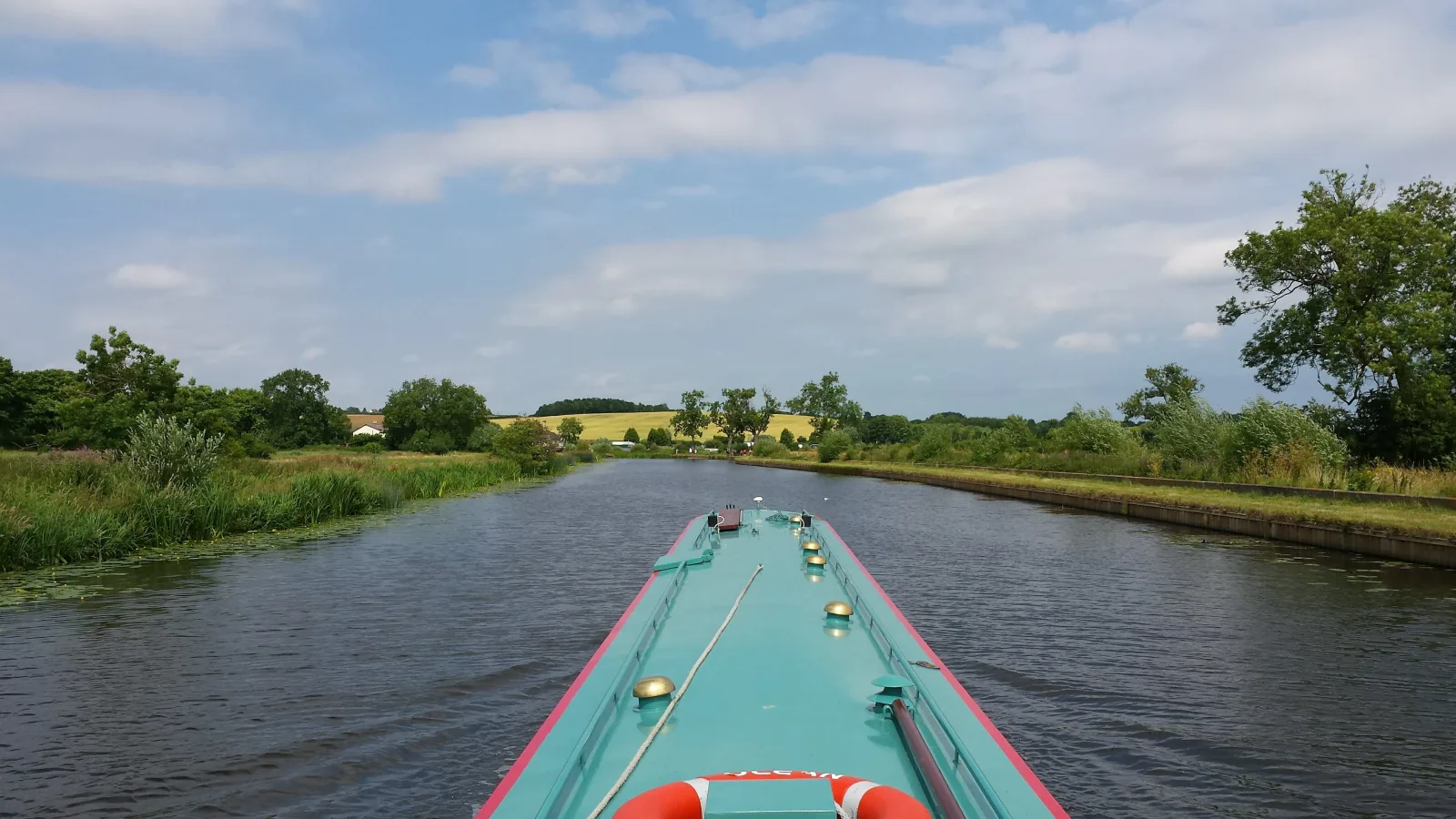 View along the canal over the bow of a narrowboat through flat open countryside