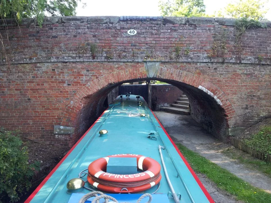 View over a lifebuoy on the bow of a narrowboat entering a brick bridge hole