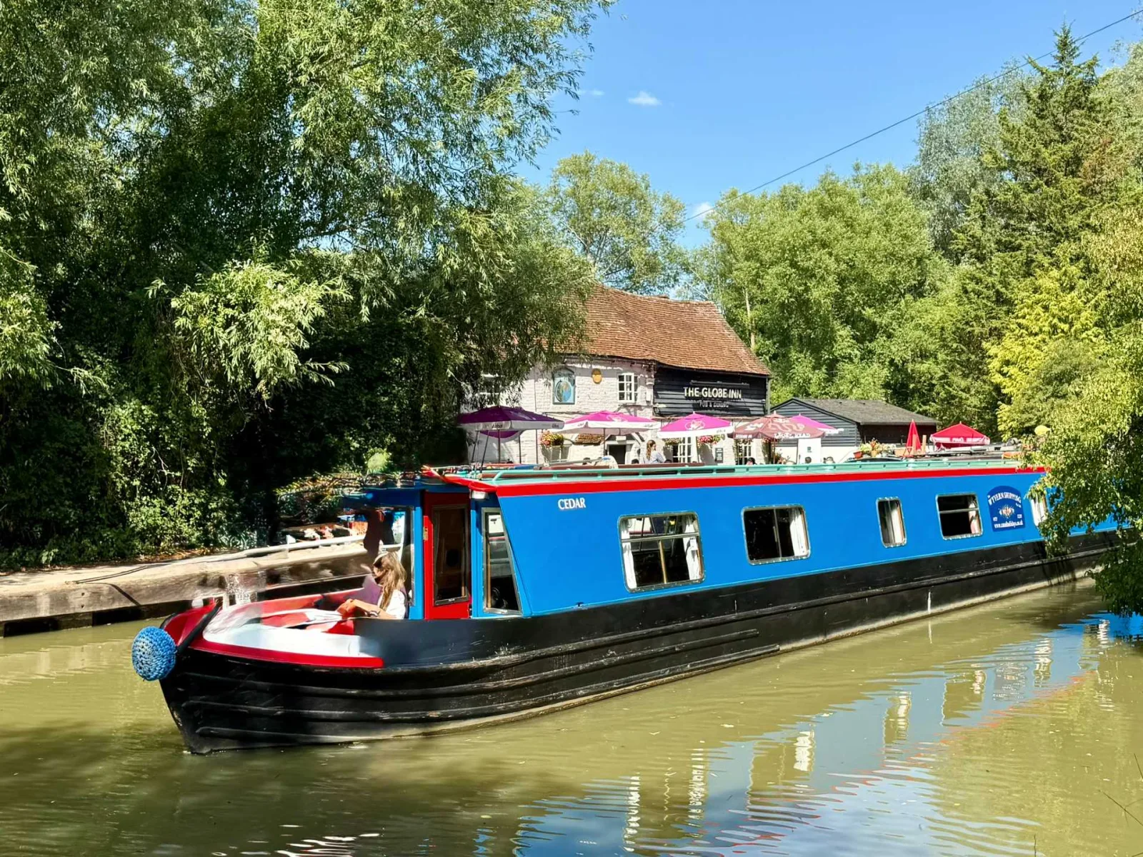 Blue narrowboat moored outside the Globe Inn on the Grand Union Canal