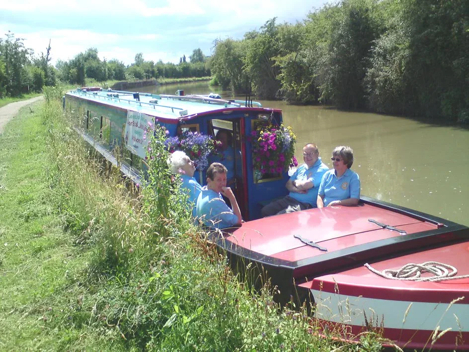 Group of people sitting on the stern of a narrowboat cruising a tree-lined canal
