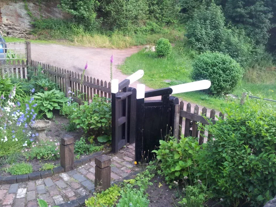 Lock gate balance beam beside a planted towpath garden and a fence