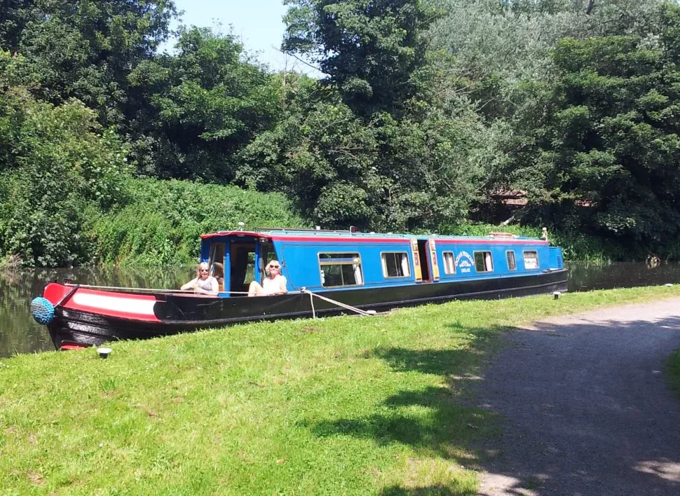 Blue narrowboat moored on the towpath in the sunshine with trees behind