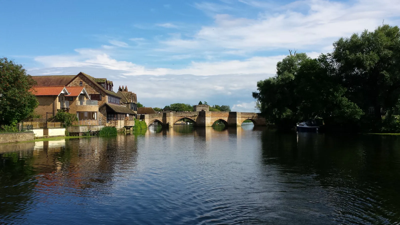 Old stone bridge crossing a wide river with buildings and trees on the far bank