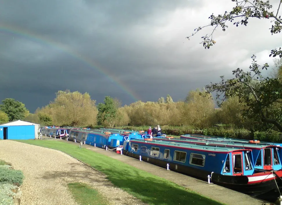 Rainbow over the Wyvern boatyard with narrowboats moored in a line along the bank