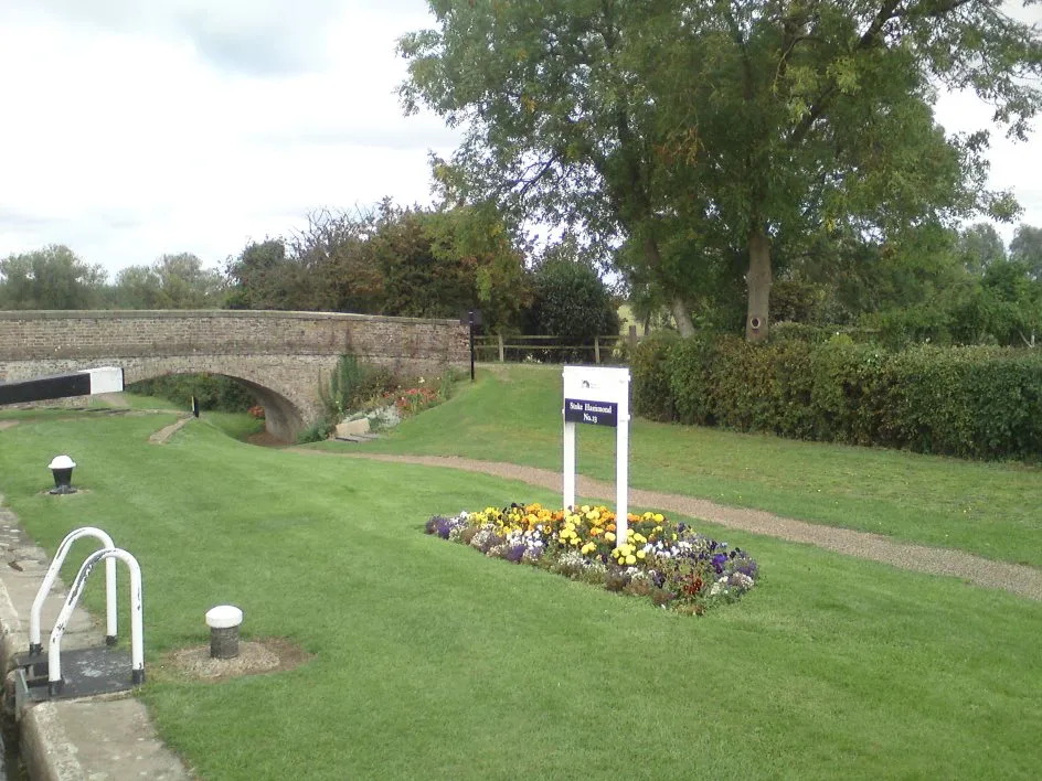 Stone canal bridge beside a mown lawn and flower bed with a mooring bollard in front