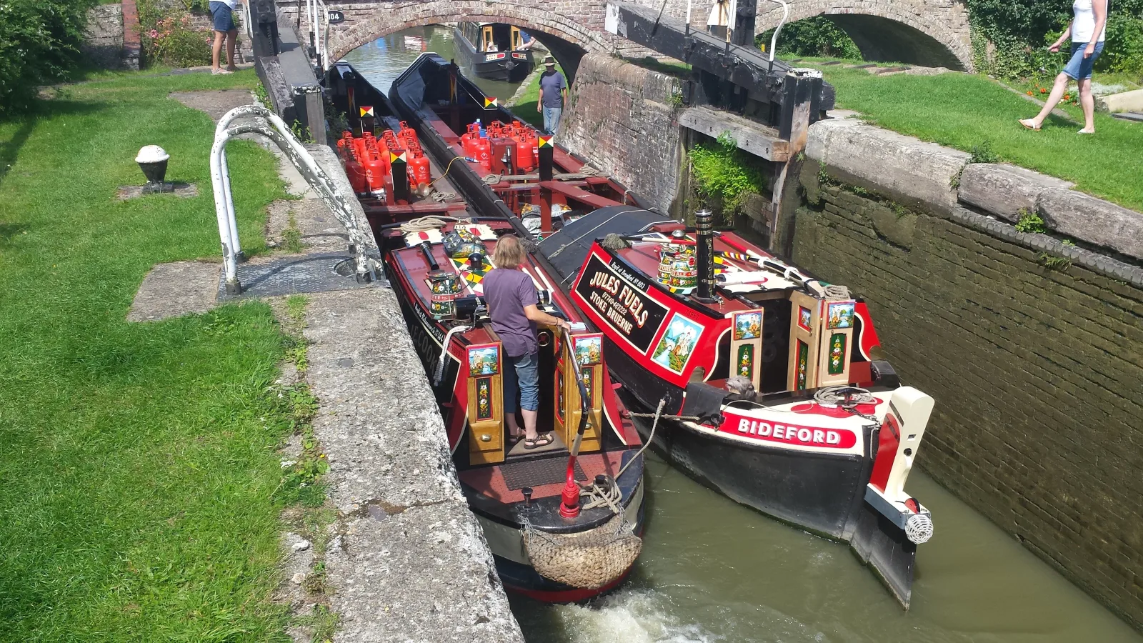 Two traditional painted narrowboats side by side in a lock below a bridge
