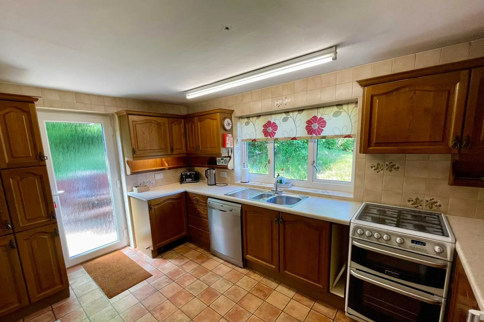 Kitchen at Waterside Cottage with wooden units an electric cooker and a tiled floor