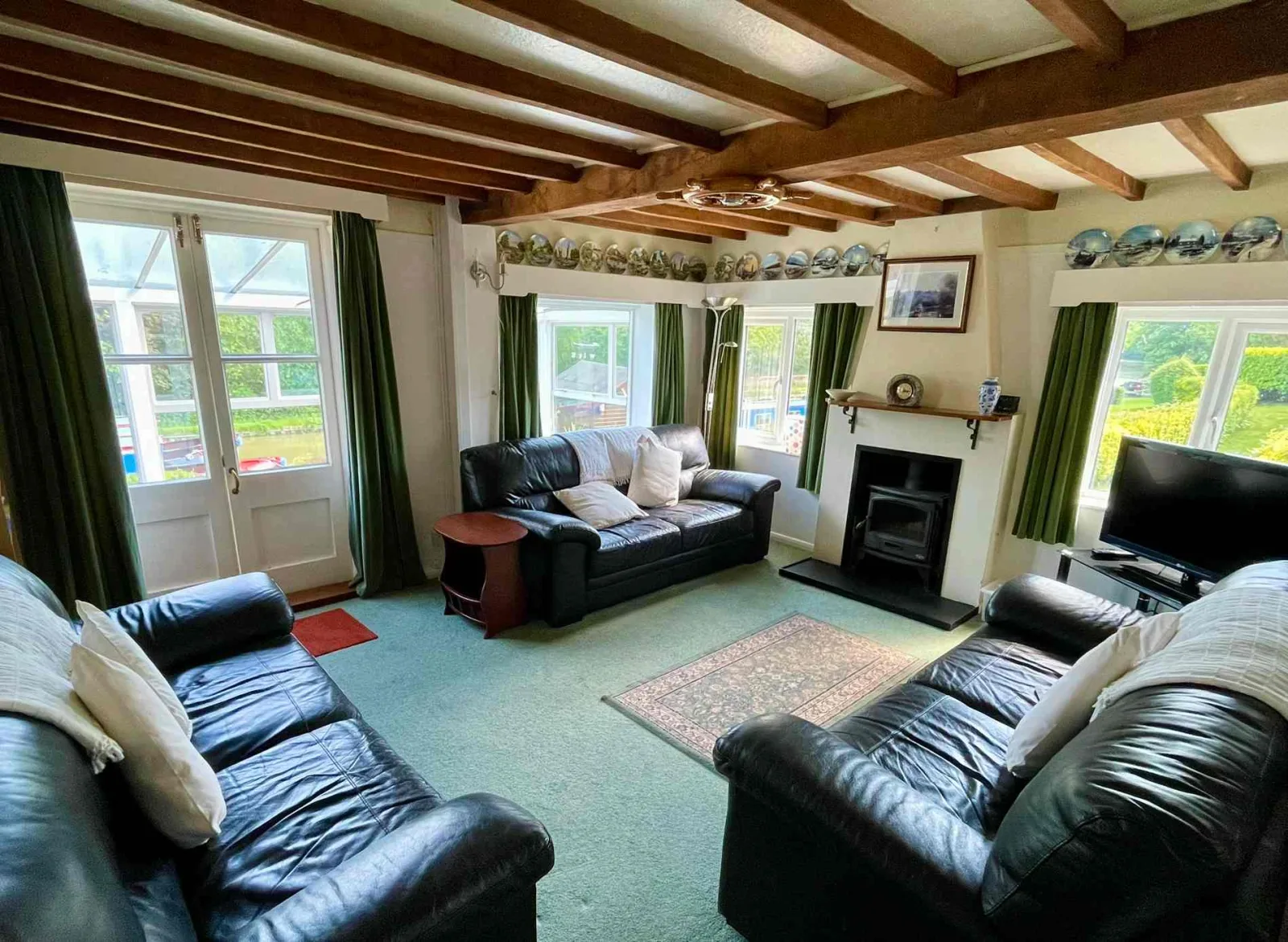 Living room at Waterside Cottage with leather sofas a fireplace and a beamed ceiling