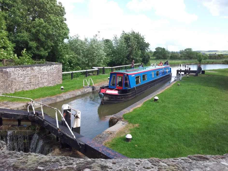 Blue narrowboat entering a lock beside a stone wall with the gates open