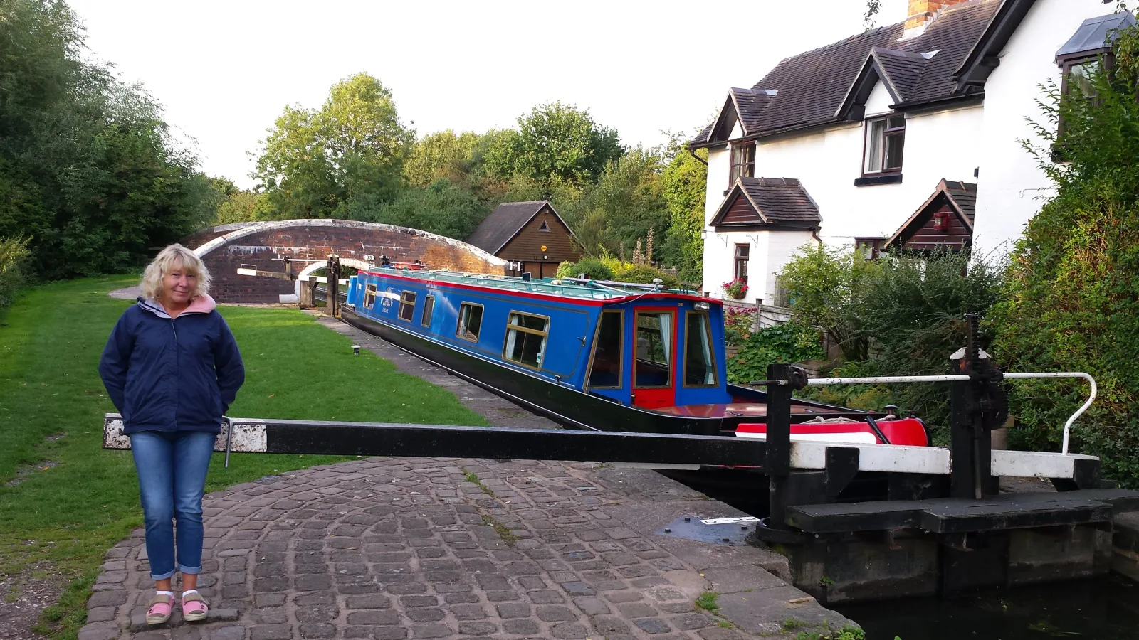 Woman on the towpath beside a blue narrowboat in a lock with a lock cottage behind
