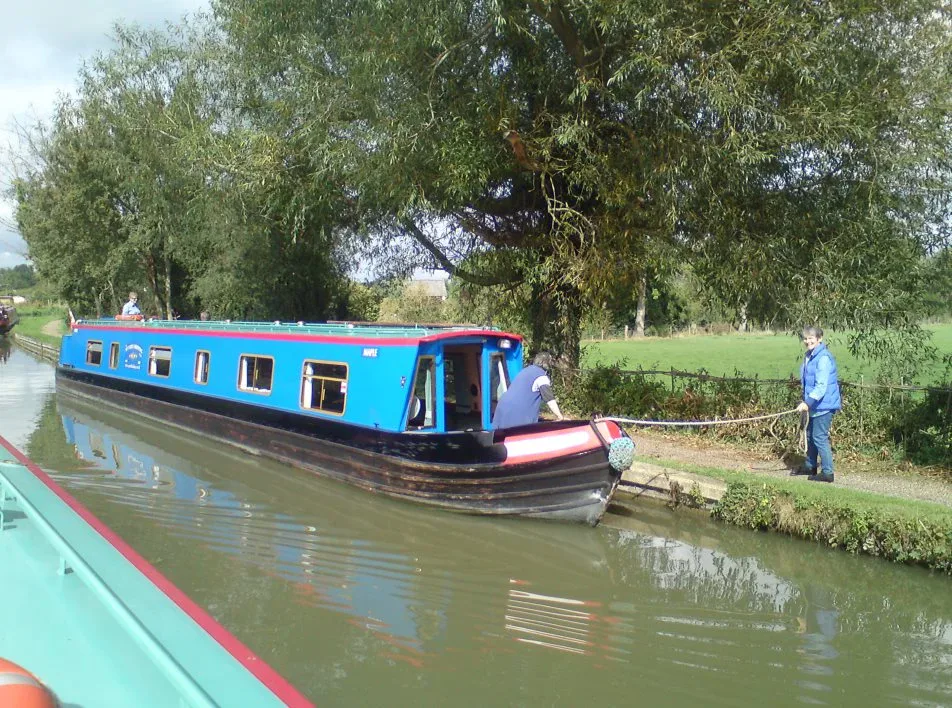 Blue narrowboat moored on the towpath with a crew member handling a rope