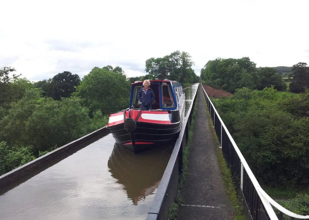 Blue narrowboat crossing a canal aqueduct with railings on both sides