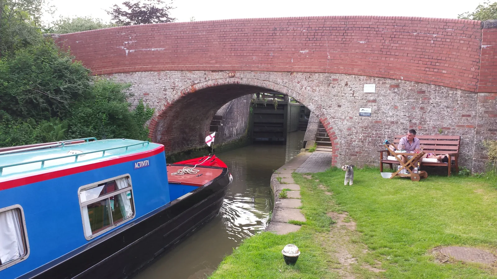 Blue narrowboat moored on the grass beside a red brick canal bridge